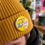 Racism Is Not Patriotism badge- Cats Against Fascism- Racism is not Patriotism Button Pin Badge, UK Political Merch, Yellow Badge with angry cat saying "Racism is not Patriotism" with Cats Against Fascism Text and Logo above Mock up on Beanie Hat