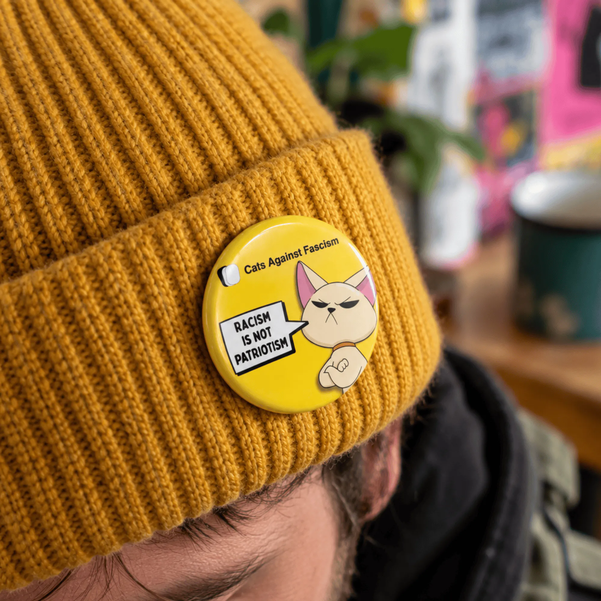 Racism Is Not Patriotism badge- Cats Against Fascism- Racism is not Patriotism Button Pin Badge, UK Political Merch, Yellow Badge with angry cat saying "Racism is not Patriotism" with Cats Against Fascism Text and Logo above Mock up on Beanie Hat